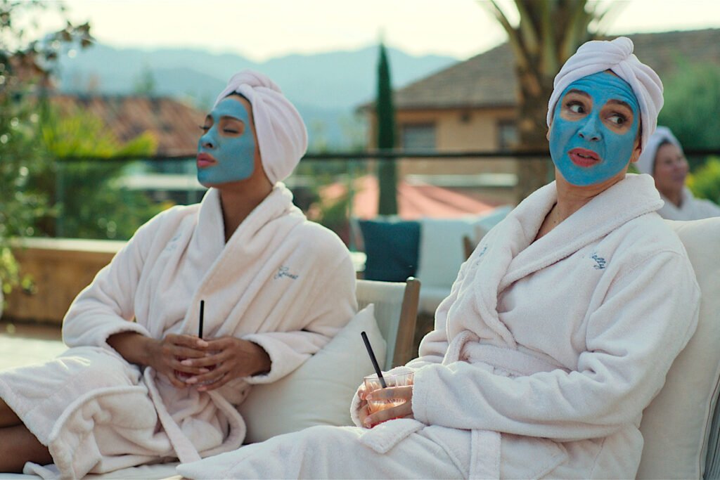 Zwei Frauen in weissen Bademänteln und mit blauen Gesichtsmasken auf Liegestühlen.