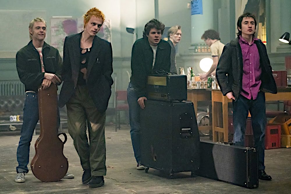 Vier junge Männer mit zwei Koffern für Musikinstrumente und einem Verstärker.