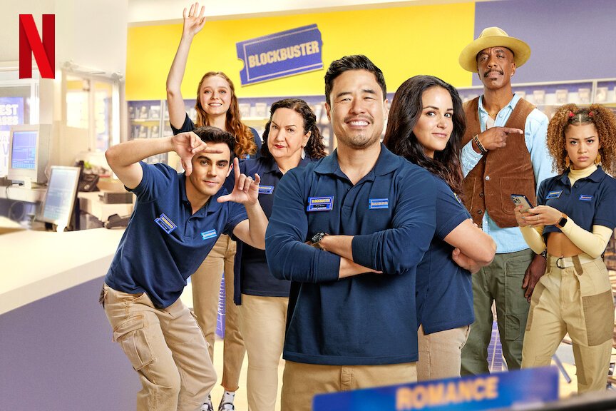 Serienposter. Sieben Personen stehen in einem Laden. Sie tragen mit einer Ausnahme alle blaue T-Shirts und beige Hosen sowie Namensschilder.