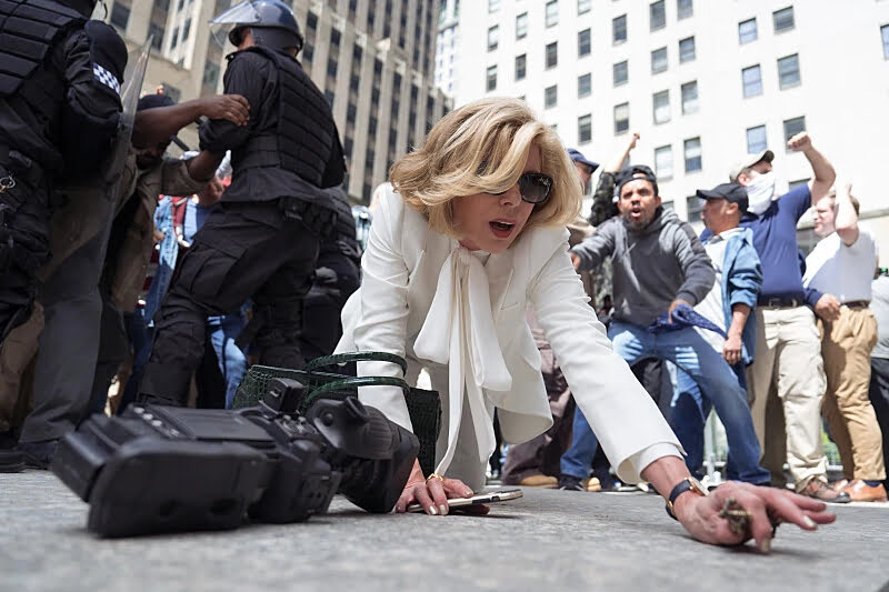 Eine Frau kniet am Boden. Im Hintergrund aufgebrachte Protestierende und Polizisten.