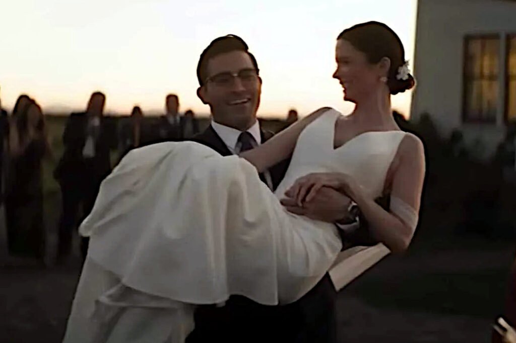 Ein Mann trägt eine Frau in weissem Brautkleide auf den Armen.
