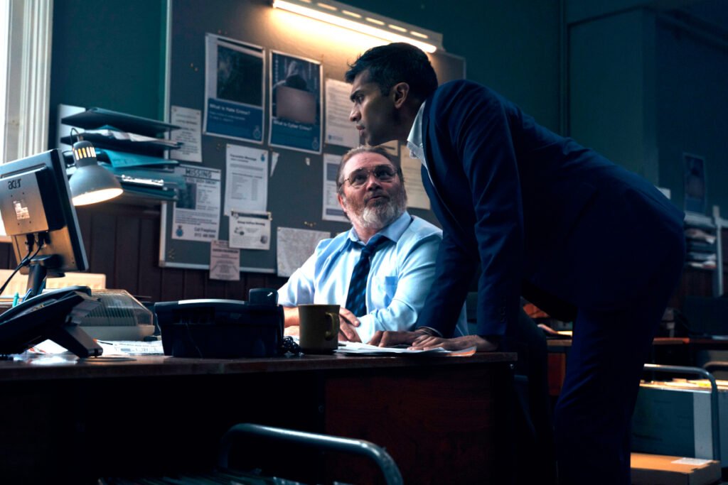 Ein Mann sitzt im Büro vor einem Computer. Ein zweiter Mann steht neben ihm und schaut auf den Bildschirm. 