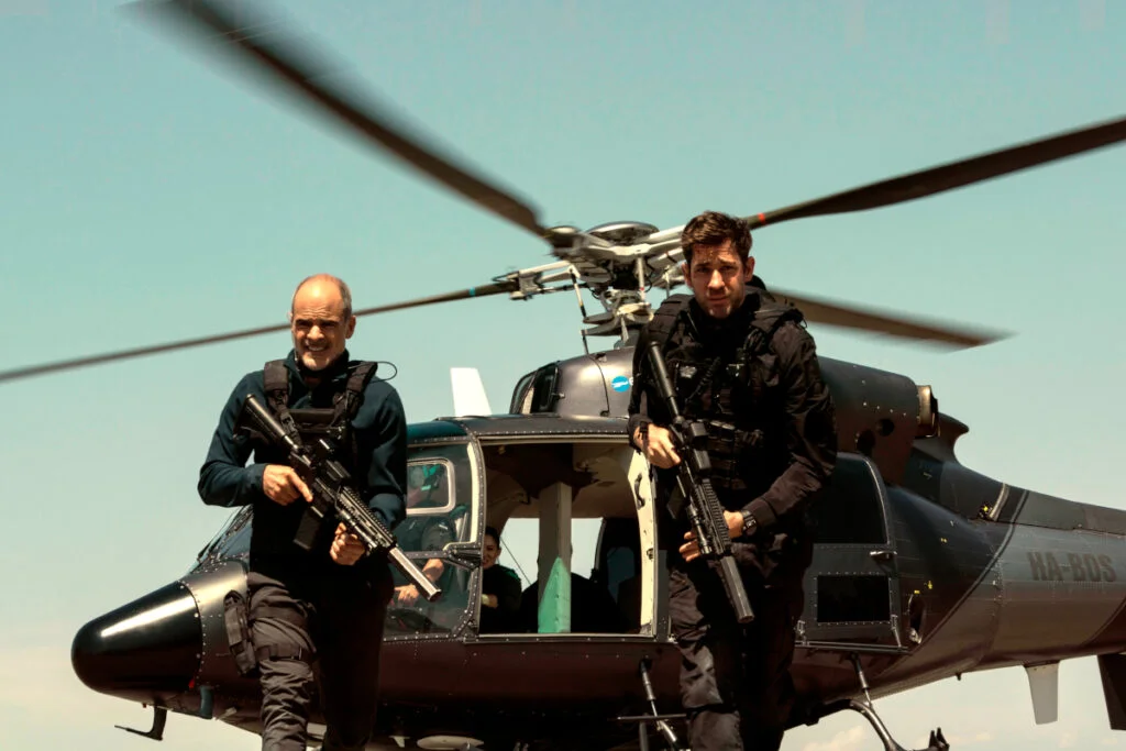 Zwei Männer in Kampfmontur und mit Waffen in den Händen vor einem Hubschrauber.