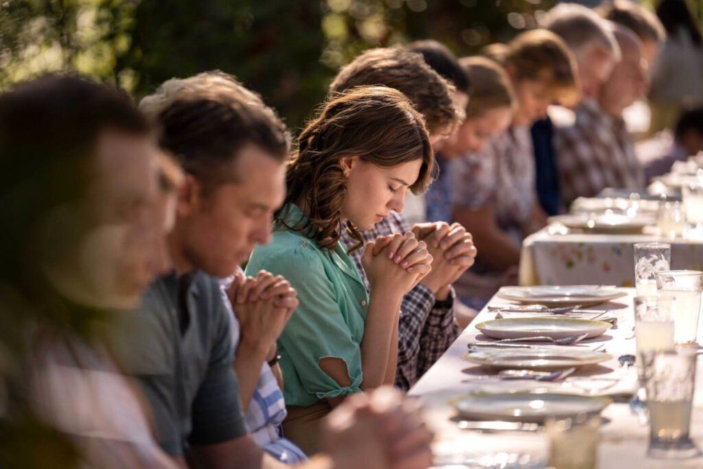 Mehrere Menschen sitzen an einem gedeckten Tisch und haben die Hände zum Gebet gefaltet.