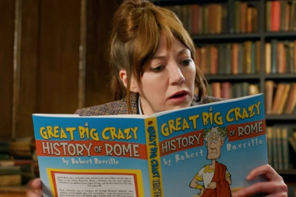 Eine Frau liest ein Comicbuch mit dem Titel «Great Big Crazy History of Rome». Im Hintergrund ein Bücherregal.
