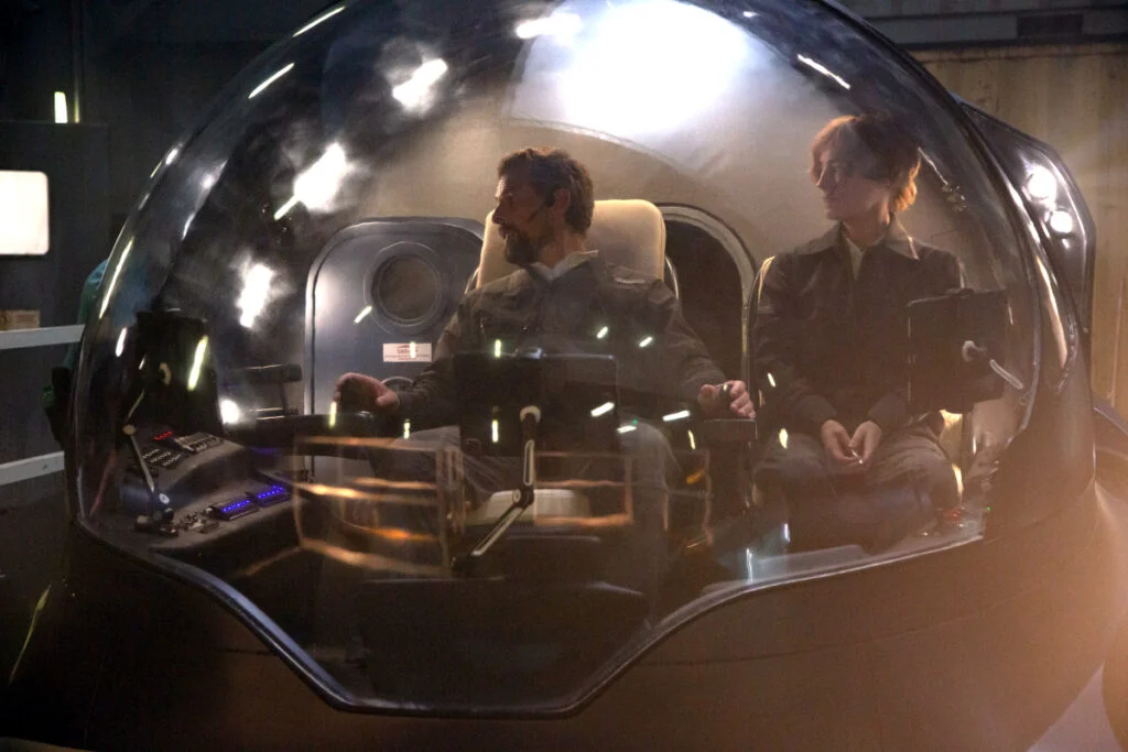 Luther Roscovitz (Klaas Heufer-Umlauf) und Charlie Wagner (Leonie Benesch) sitzen in einem kleinen Uboot. Das Uboot ist rund und hat eine große Glasscheibe mit Beleuchtung an beiden Seiten.