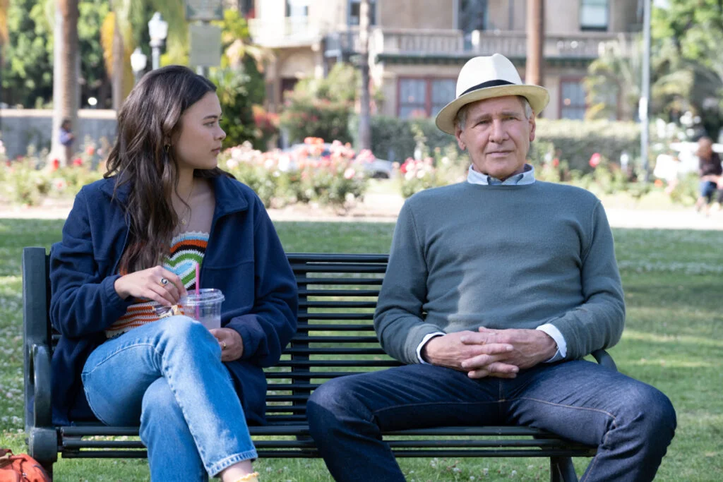 Eine junge Frau und ein älterer Mann mit weissem Hut sitzen auf einer Parkbank.