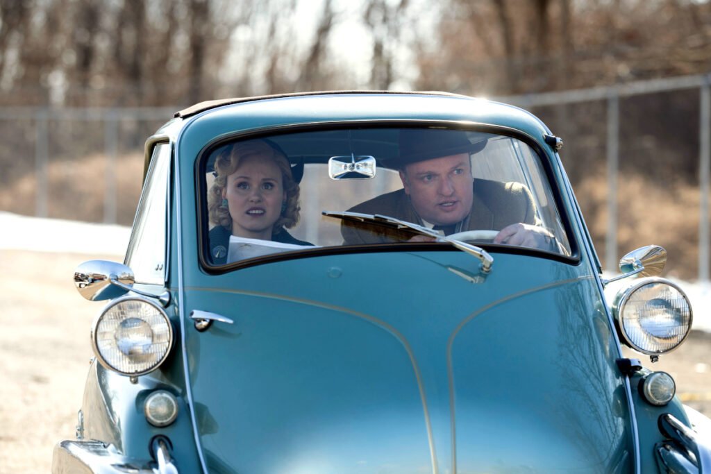 Eine Frau und ein Mann sitzen in einem kleinen Auto mit Fronttüre.