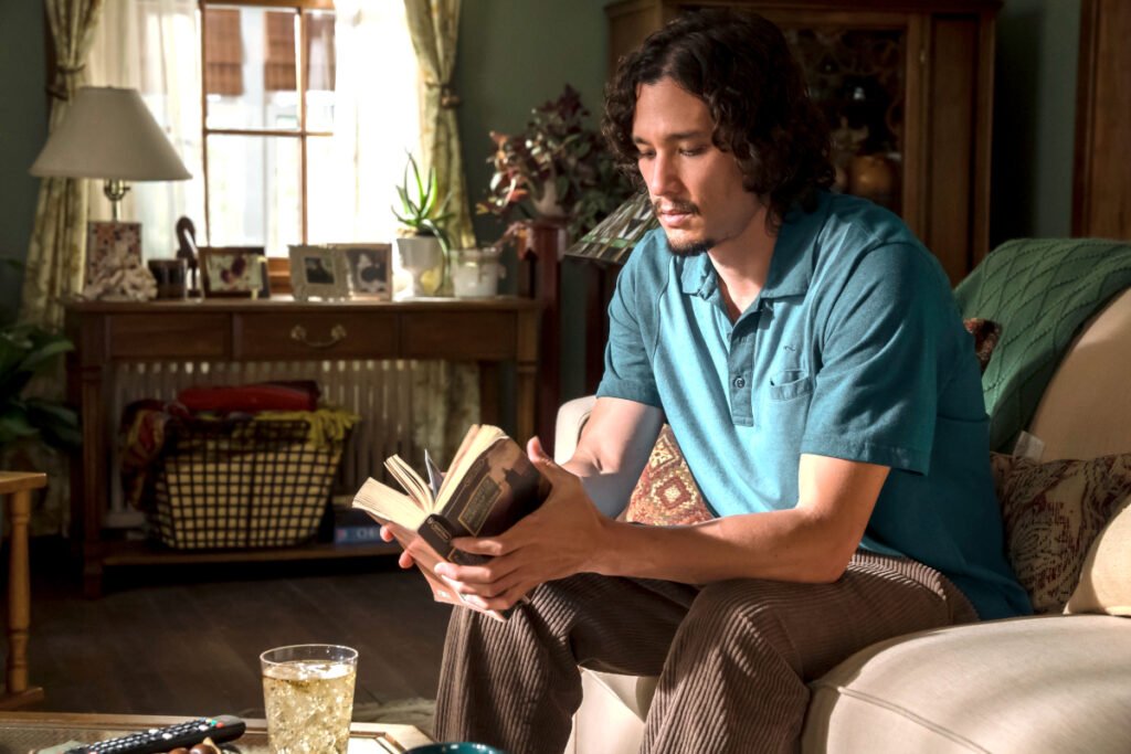 Ein junger Mann sitzt auf einem Sofa und hält ein Buch in den Händen.