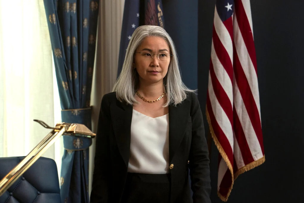 Eine Frau mit weissen langen Haaren steht hinter einem Bürotisch. Hinter ihr die US-amerikanische Flagge.
