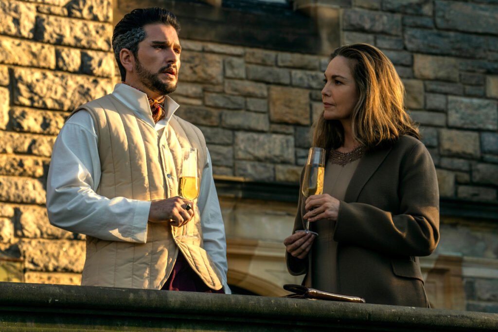 Ein Mann und eine Frau stehen auf einer Terrasse vor einer Steinmauer mit Champagnergläsern in der Hand.