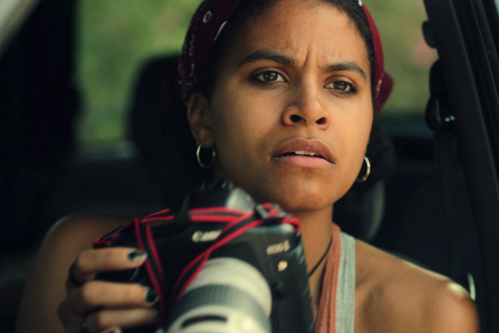 Eine Frau hält eine Kamera mit Zoomobjektiv in der Hand und blickt konzentriert in die Ferne.