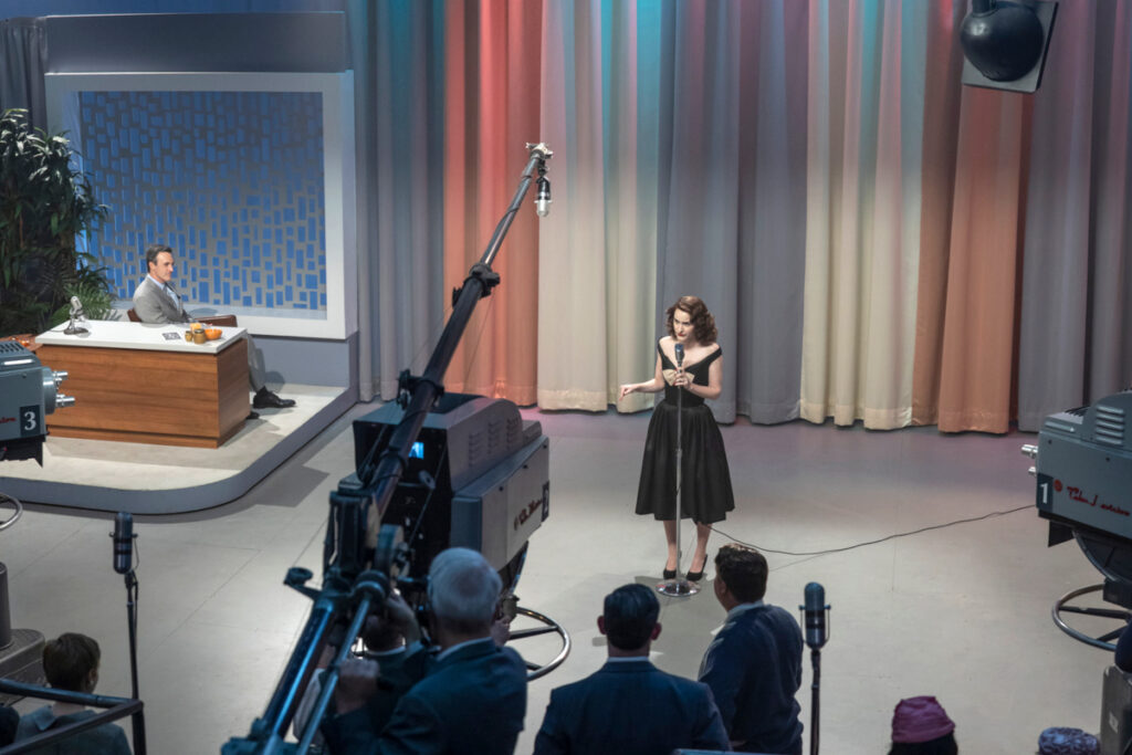 Eine Frau steht in einem TV-Studio vor einem Mikrofon. Die Kameras sind auf sie gerichtet.