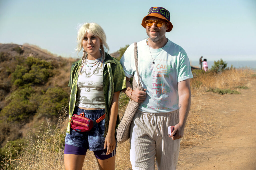 Eine junge blonde Frau mit einem bärtigen Mann beim Spazieren auf einer Anhöhe. 
