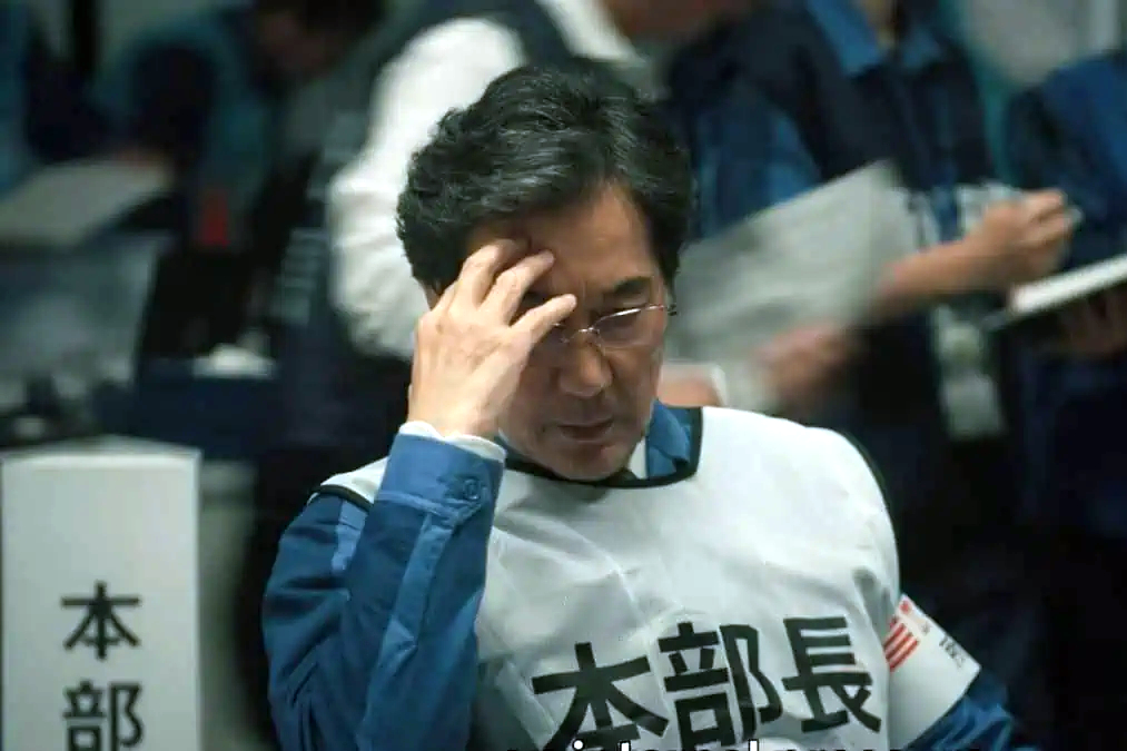 Ein Mann hat seinen Kopf auf seine Hand abgestützt. Er trägt eine Weste mit japanischer Beschriftung.