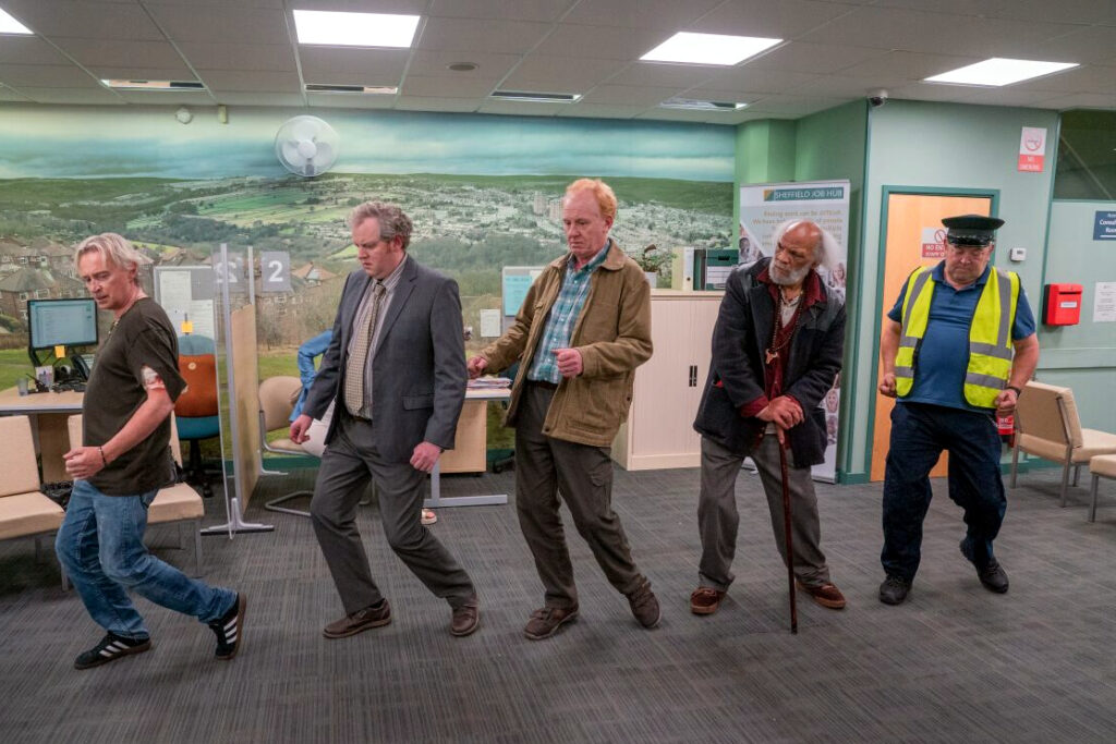 Fünf ältere Männer in einem Grossraumbüro, die Tanzschritte machen.