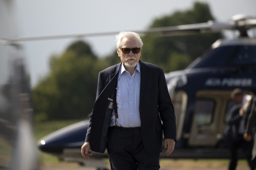Ein älterer Mann mit weissem Bart und Sonnenbrille vor einem Helikopter.
