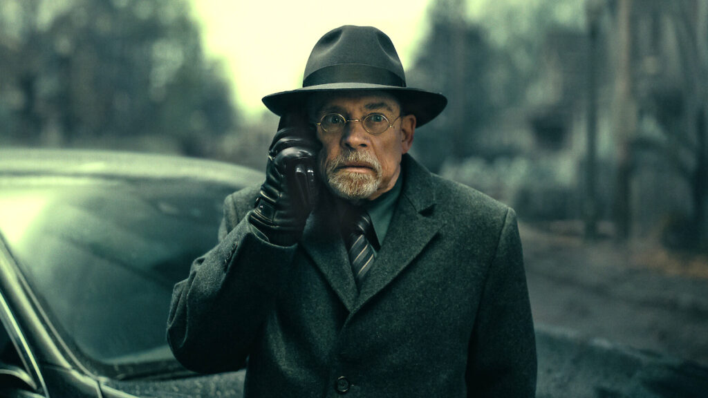 Ein älterer Mann mit Hut und Mantel. Er telefoniert mit einem Handy.