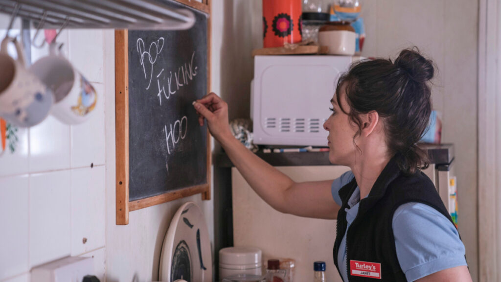 Eine Frau schreibt in der Küche eine kurze Abschiedsbotschaft auf eine Wandtafel.