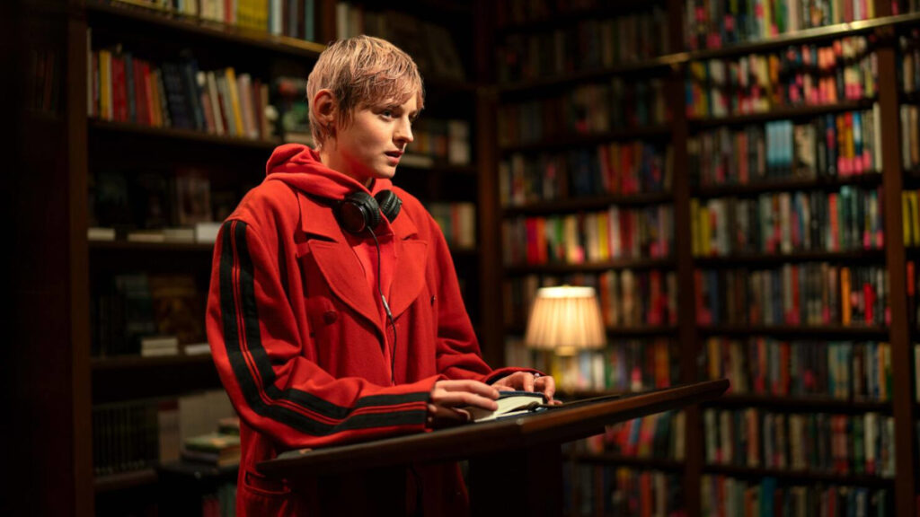 Eine junge Frau in roter Jacke steht an einem Pult in einer Buchhandlung und liest vor.