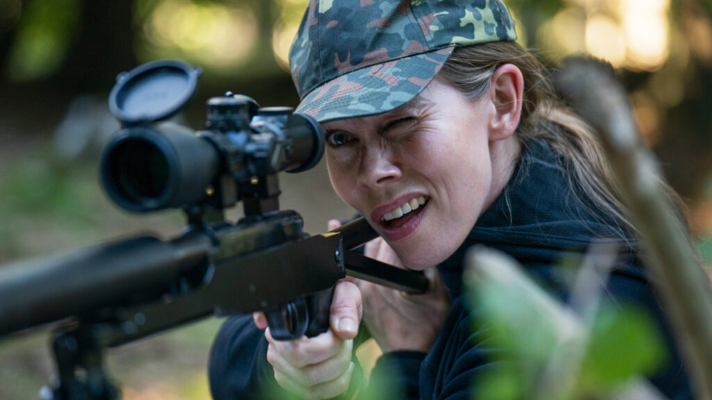 Eine Frau mit Tarnkappe an einem Gewehr mit Zielfernrohr.