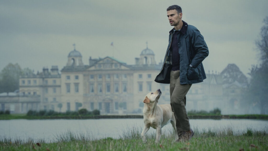 Ein Mann spaziert mit Hund an einem See. Im Hintergrund ein grosses Anwesen.