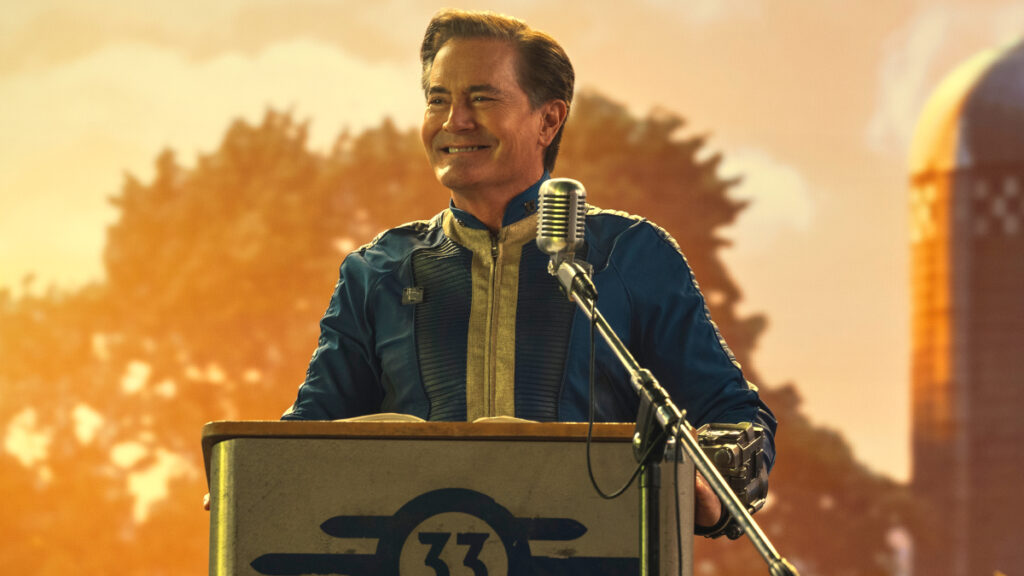 Ein Mann in einem blauen Overall steht an einem Rednerpult und lächelt. 