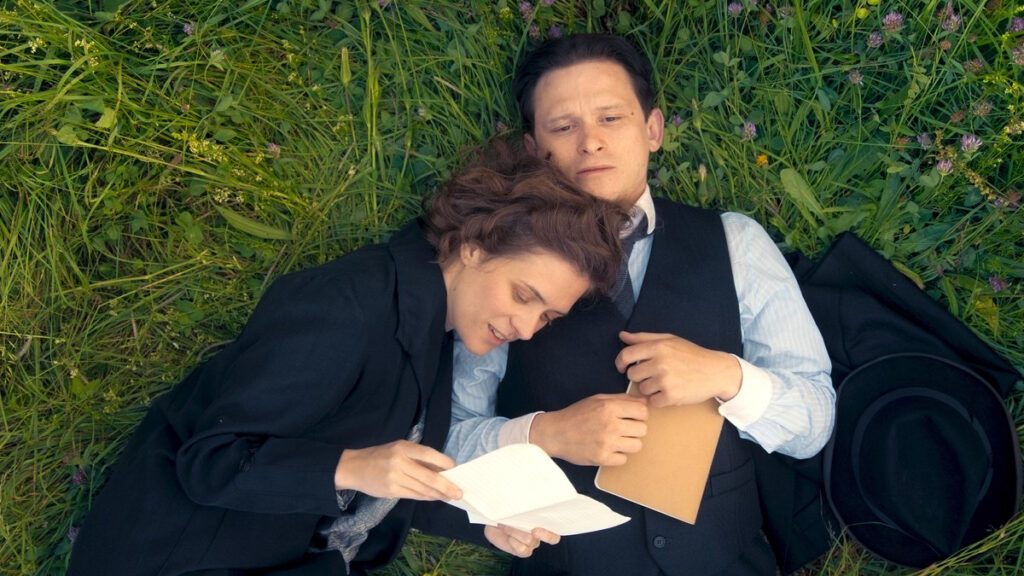 Ein Mann liegt auf einer grünen Wiese, eine Frau neben ihm, den Kopf auf seine Schulter gelegt. Sie liest einen Brief.
