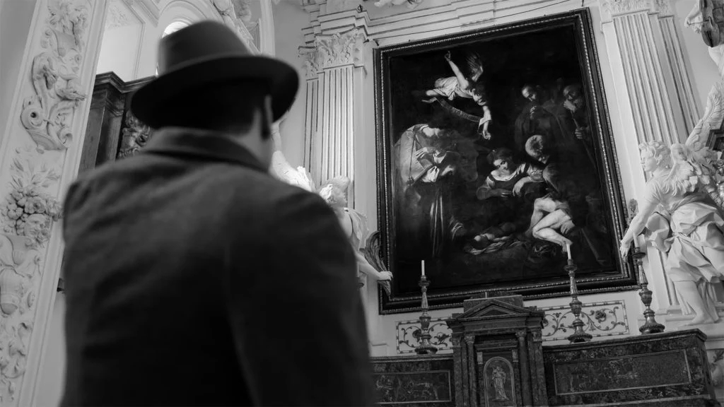 Ein Mann mit Hut steht vor einem grossen Gemälde.