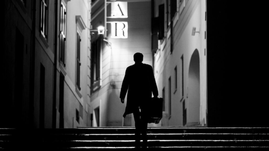 Der Schatten eines Mannes auf einer Treppe unterwegs zu einer hell leuchtenden Lichtreklame.