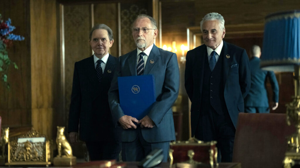 Drei Männer in Anzügen stehen vor einem Schreibtisch.