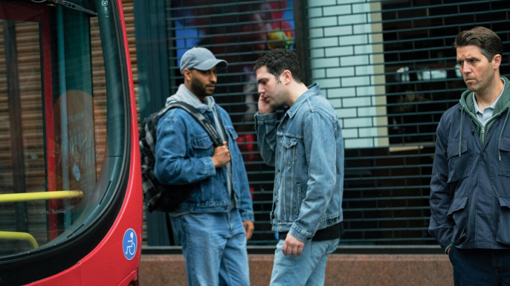 Ein Mann in Jeansjacke auf der Strasse telefoniert. Zwei andere Männer beobachten ihn.