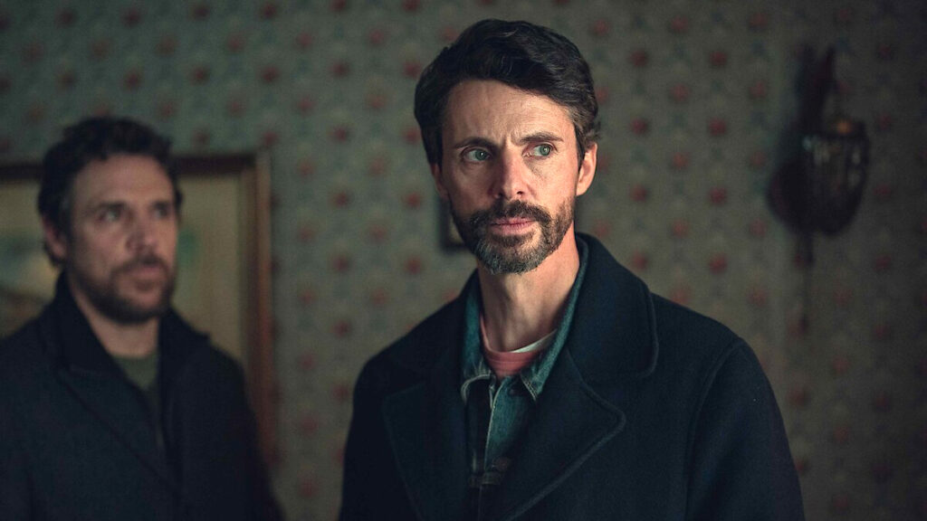 Ein Mann in einer Wohnung, unscharf im Hintergrund ein zweiter Mann.