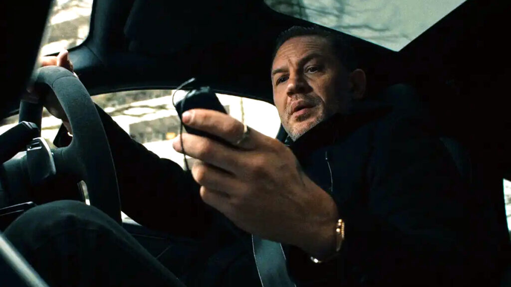 Ein Mann am Steuer eines Autos. Er blickt auf sein Handy.