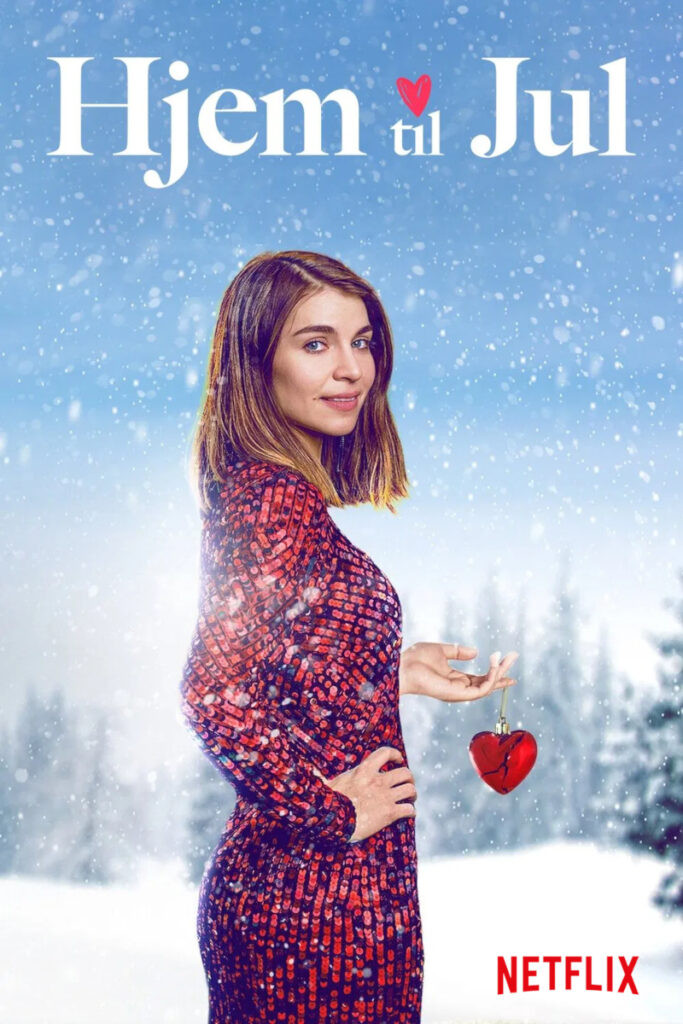 Eine Frau in einem roten Kleid steht im Schnee. Sie hält ein rotes Herzornament in der Hand. Oben steht der Titel «Hjem til Jul». Im Hintergrund sind verschwommene verschneite Bäume zu sehen. Das Netflix-Logo ist unten rechts platziert.