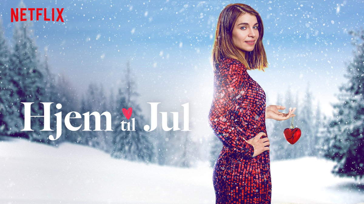 Eine Frau in einem roten Kleid steht vor einer verschneiten Winterlandschaft. Sie hält ein rotes Herzornament. Schneeflocken fallen sanft. Das Netflix-Logo ist oben links zu sehen. Der Titel «Hjem til Jul» steht gross im Vordergrund.