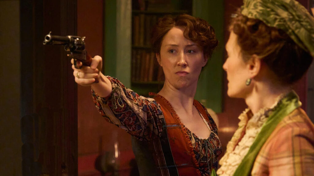 Eine Frau in historischer Kleidung zielt mit einer Pistole. Eine zweite Frau steht im Vordergrund, teilweise im Profil.