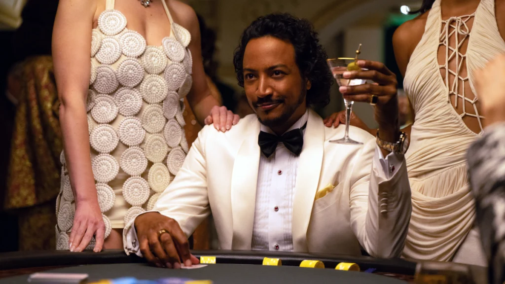 Eine elegant gekleidete Person sitzt an einem Spieltisch, umgeben von zwei anderen Personen in stilvollen Kleidern. Sie hält ein Cocktailglas in der Hand und wirkt zufrieden. Alle tragen formelle Abendgarderobe, was auf ein gehobenes Ambiente hinweist.