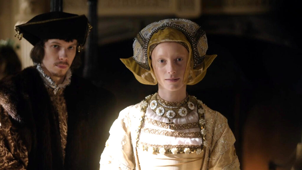 Zwei Personen in historischer Kleidung stehen nebeneinander in einem dunklen Raum.