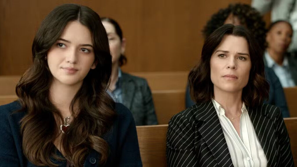 Zwei Frauen sitzen nebeneinander in einem Gerichtssaal. Die linke Frau trägt einen dunkelblauen Blazer und hat lange, wellige braune Haare. Die rechte Frau trägt einen gestreiften Blazer über einer weissen Bluse und hat schulterlange braune Haare. Beide blicken ernst nach vorn.