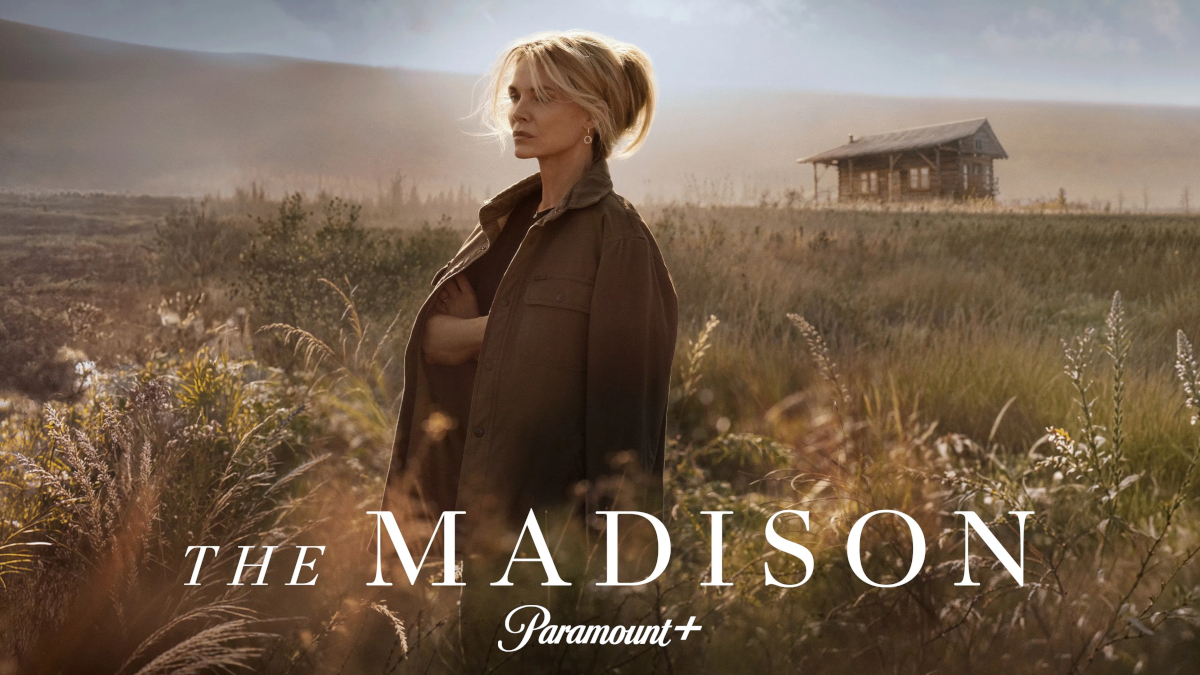 Blonde Frau in brauner Jacke steht in goldener Abendstimmung auf einer Wiese mit hohem Gras. Im Hintergrund ist ein rustikales Holzhaus zu sehen. Unten im Bild der Serientitel «The Madison» mit dem Paramount+ Logo.