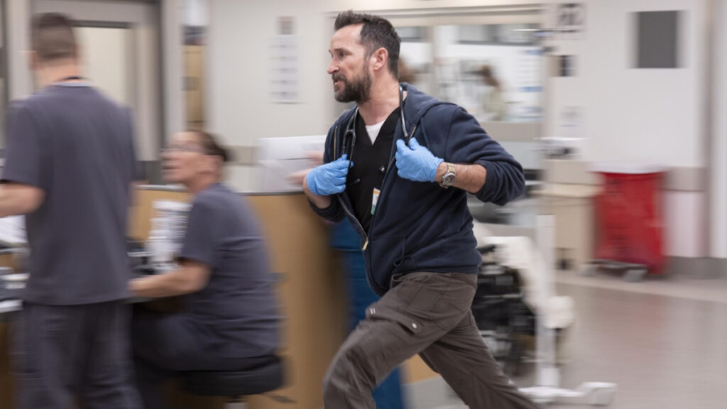 Ein Arzt mit Stethoskop und blauen Handschuhen rennt durch einen Krankenhausflur. Die Bewegungsunschärfe im Hintergrund vermittelt Hektik und Dringlichkeit in der medizinischen Notfallsituation.
